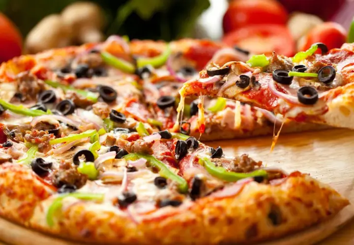 Pyszna pizza z gotowego ciasta, obficie posypana serem, oliwkami, papryką i mięsem. Ser ciągnie się apetycznie.