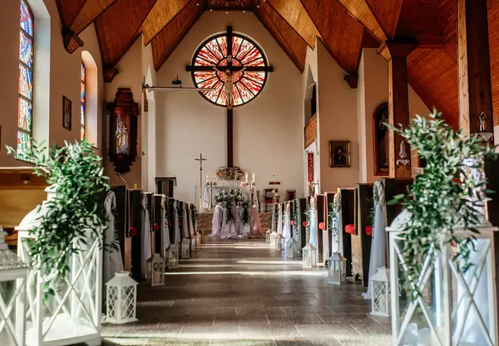 Piękna dekoracja kościoła na ślub samemu: ławki ozdobione zielenią i lampionami, ołtarz z kwiatami.