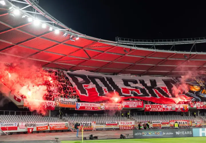 Tłum ultrasi na stadionie, odpalone race i ogromny transparent "POLSKA".