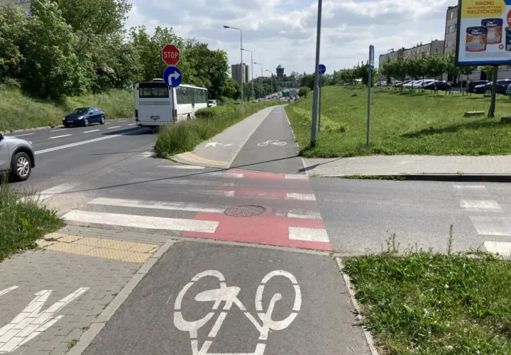 Przejście dla pieszych na ścieżce rowerowej, z oznaczeniem roweru. Autobus i samochody czekają na drodze.