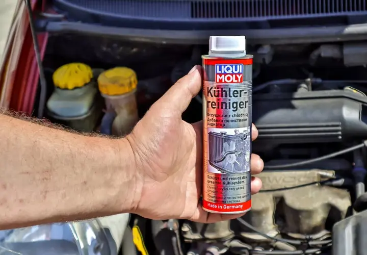 Dłoń trzyma puszkę środka do czyszczenia układu chłodzenia Liqui Moly. W tle widać silnik samochodu.