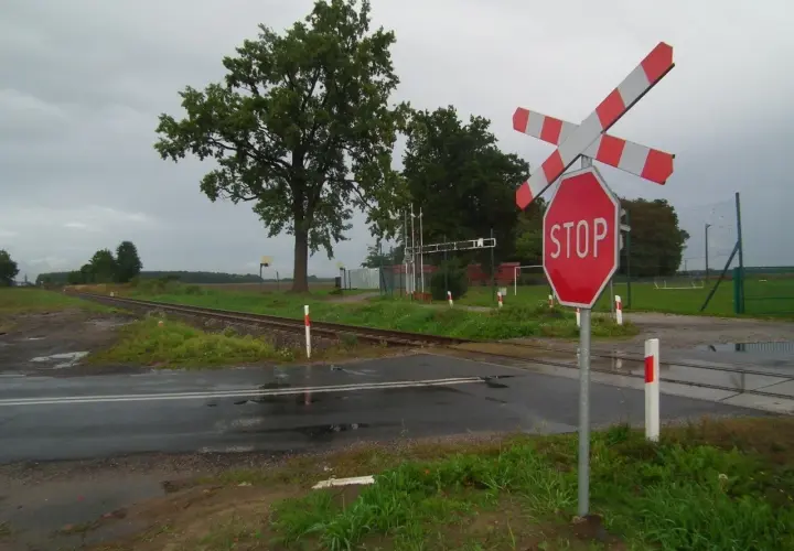 Wielotorowy przejazd kolejowy z czerwonym znakiem STOP i rogatkami.