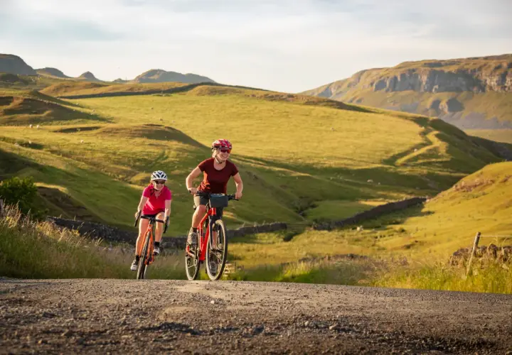 Two women enjoy a scenic ride on their bikes through rolling green hills, a perfect example of England bike tours.
