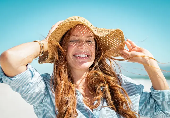 Mujer sonríe bajo sombrero de paja, con el pelo suelto. Consejos para como cuidar el pelo en verano.