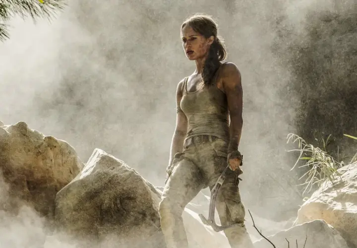 Alicia Vikander jako Lara Croft, wspinająca się po skalistym terenie, otoczona pyłem i mgłą.