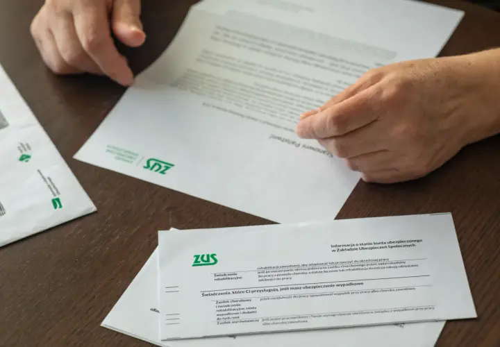 Dłonie przeglądają dokumenty ZUS. Informacje o świadczeniach i tym, jak przejść na emeryturę, są kluczowe.