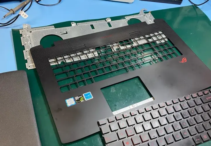 Części laptopa ROG gotowe do wymiany klawiatury. Widoczna górna obudowa z miejscem na klawisze i nowa klawiatura z czerwonymi oznaczeniami.