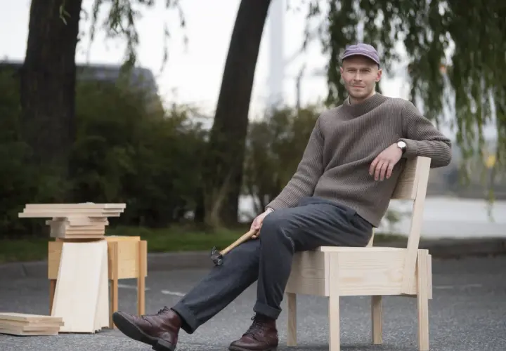 Erik Eje Almqvist sitter på en trästol med en hammare i handen, omgiven av trämaterial.