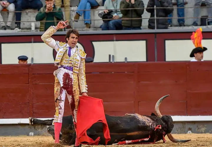 Un torero herido, con su traje manchado de sangre, se alza triunfante sobre un toro caído. La escena evoca la cruda realidad de la muerte torero.