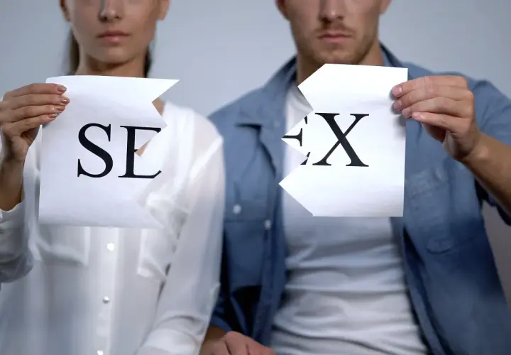 Coppia strappa fogli con lettere "SE" e "X", simboleggiando la fine di una relazione o un'assenza di intimità, forse legata al concetto di asessuale significato.
