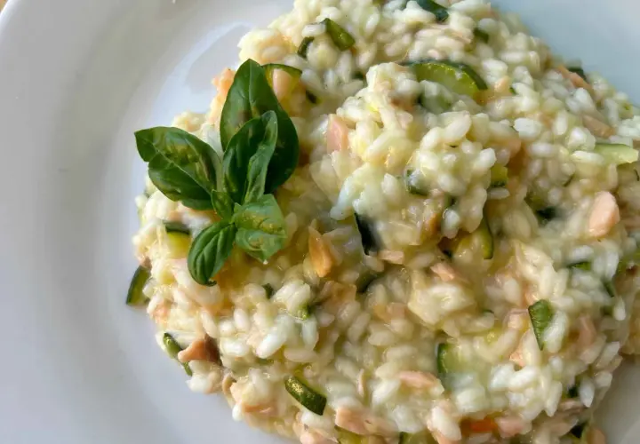 Un cremoso risotto con verdure, zucchine e pezzetti di salmone, guarnito con foglie di basilico fresco.