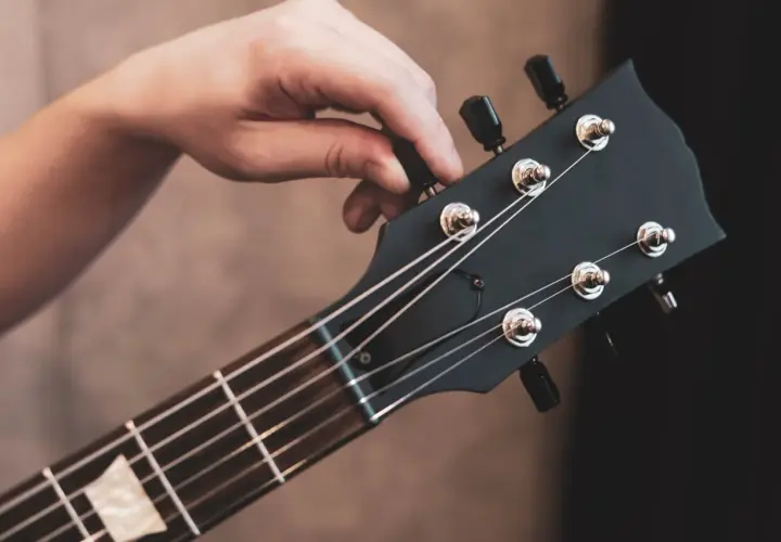 Hand tuning a black electric guitar headstock with tuning pegs and strings.