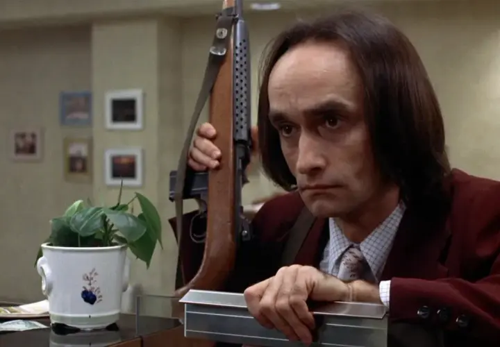 Un uomo con un fucile a tracolla, forse in una scena che ricorda il john cazale funeral, guarda intensamente.