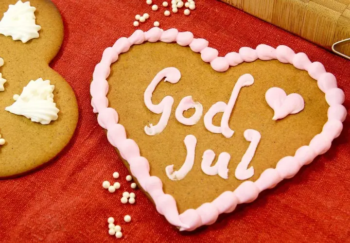 Hjärtformade pepparkakor med rosa glasyr och texten "God Jul". Bredvid syns en pepparkaka dekorerad med vita pepparkakor-liknande mönster.
