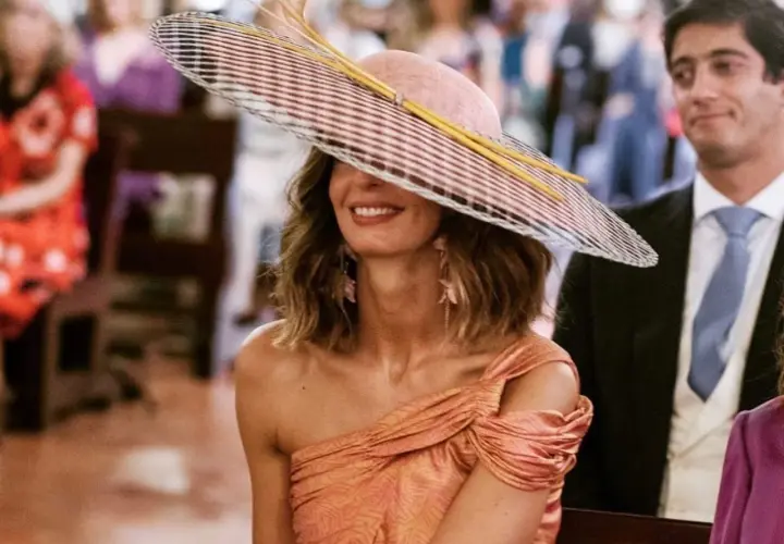 Peinado ondas invitada boda: mujer con sombrero de ala ancha y vestido naranja, sonriendo.