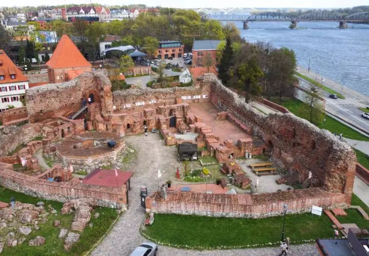 Ruiny zamku bierzgłowskiego z cegły, z widokiem na Wisłę i most.