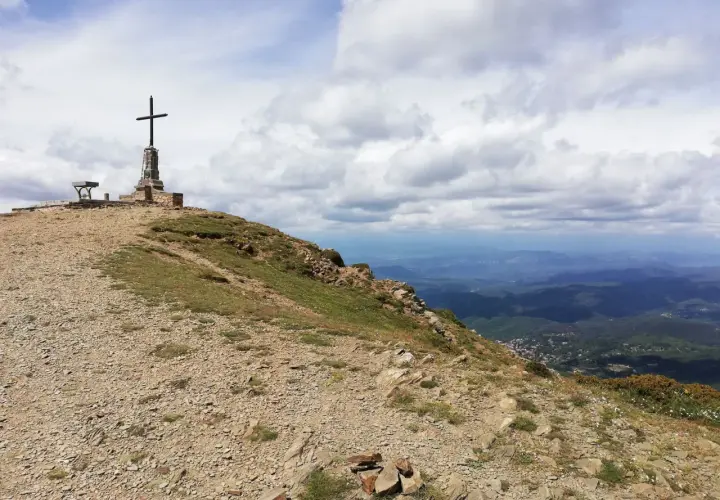 Cima de montaña con cruz y banco, ideal para **rutes per osona**. Paisaje de valles y nubes.