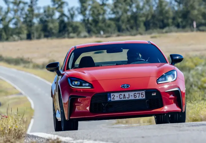 La Toyota sportiva rossa sfreccia su una strada tortuosa, con il sole che illumina il suo design aggressivo.
