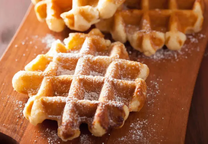 Gaufres liégeoises dorées saupoudrées de sucre glace sur une planche en bois. Un délice croustillant.