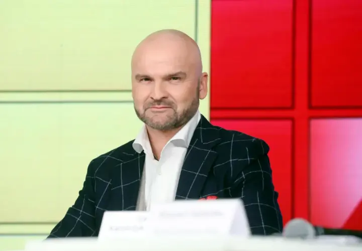 Rafał Brzoska, znany z budowania swojego majątku, w eleganckim garniturze siedzi przed ekranem.