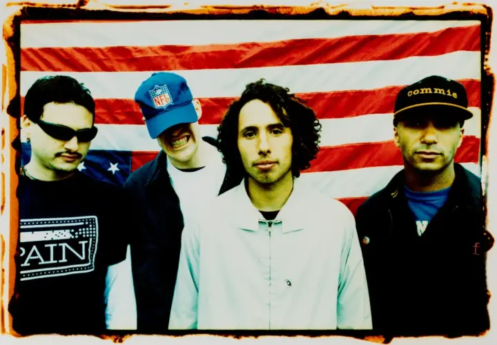Członkowie Rage Against the Machine pozują przed amerykańską flagą. Jeden z nich ma na głowie czapkę z napisem "commie".