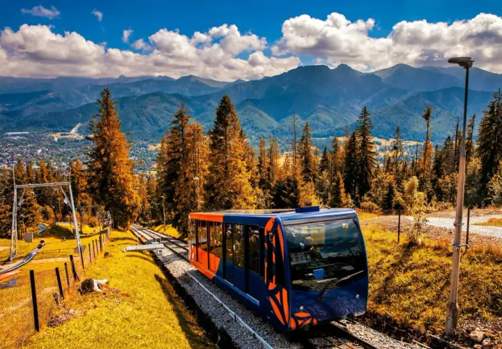 Kolejka linowa w Zakopanem pnie się wśród jesiennych drzew, oferując widok na Tatry.