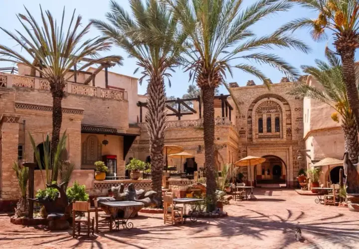 Sonniger Innenhof mit Palmen und traditioneller Architektur in der Agadir Altstadt. Tische und Stühle laden zum Verweilen ein.