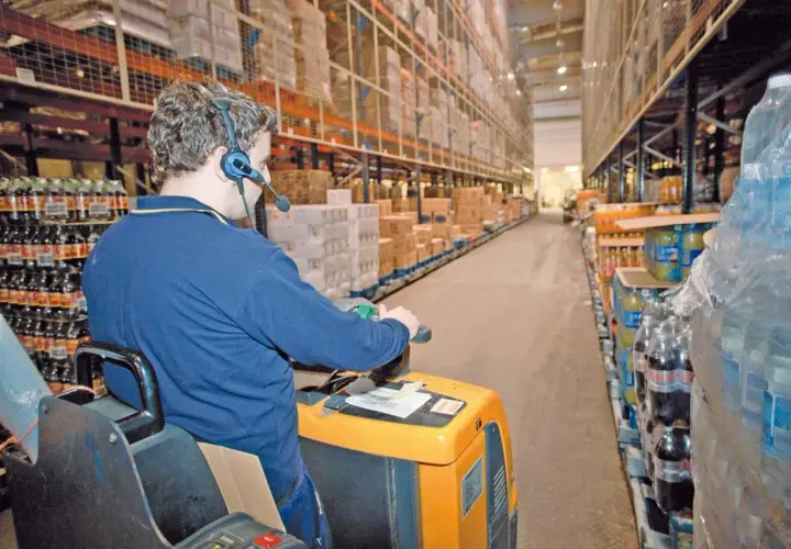 Mitarbeiter mit Headset führt Kommissionierauftrag per Sprachsteuerung (pick by voice) im Lager durch.