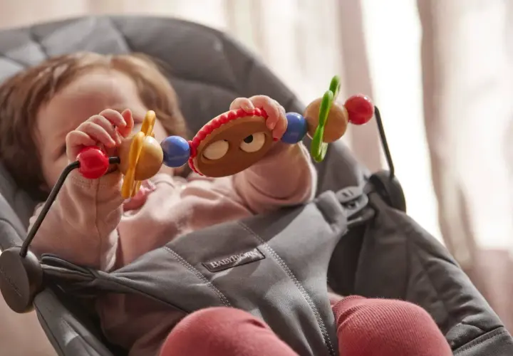 Maluch bawi się zabawką w leżaczku BabyBjorn. Od kiedy dziecko zaczyna sięgać po przedmioty, taki leżaczek jest idealny.