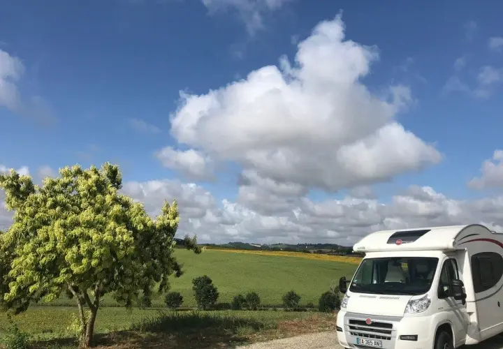 Camping-car en France, sous un ciel bleu et nuageux, avec un champ de tournesols en arrière-plan. La passion du voyage en camping-car.