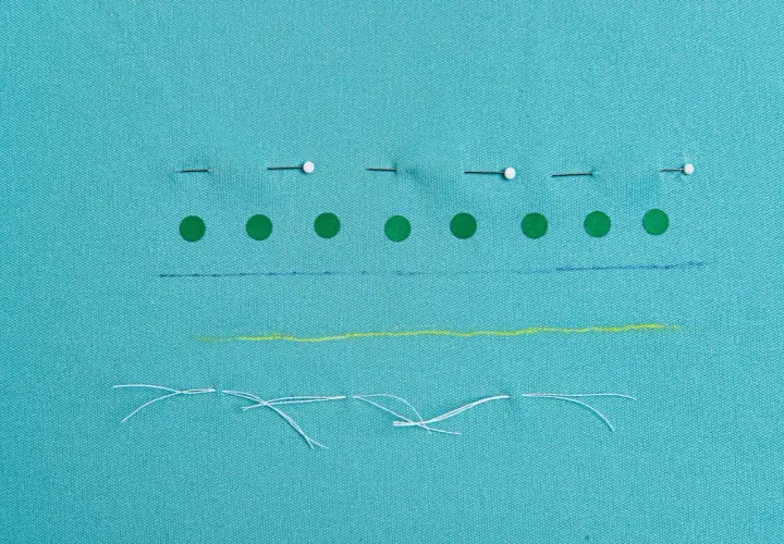 Tissu bleu turquoise avec des épingles, des ronds verts, des traits bleus, jaunes et des fils blancs.
