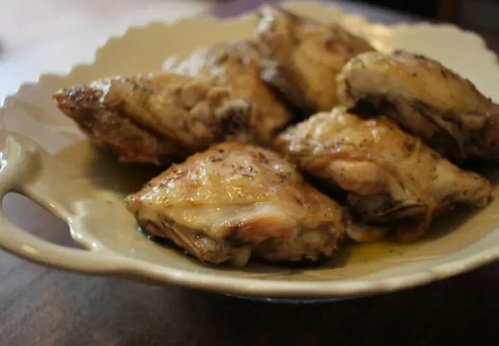 Plusieurs hauts de cuisse de poulet rôtis, assaisonnés d'herbes, reposent sur une assiette en céramique crème.
