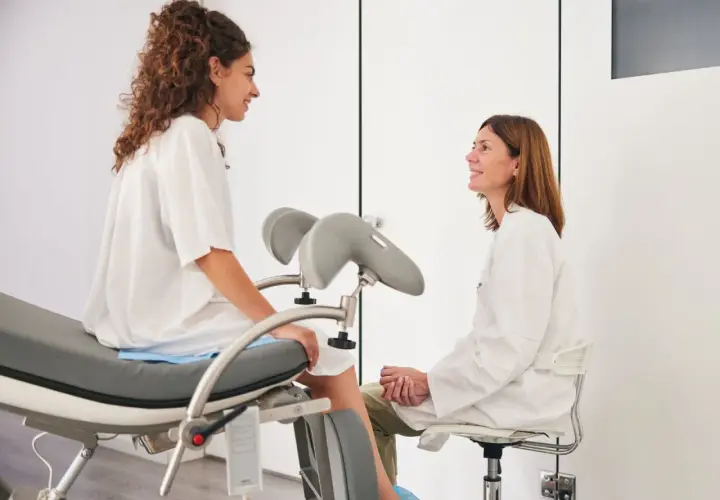 Frauenärztin im Gespräch mit Patientin auf dem gynäkologischen Stuhl. Auch während der Periode ist ein Besuch beim Frauenarzt möglich und wichtig.