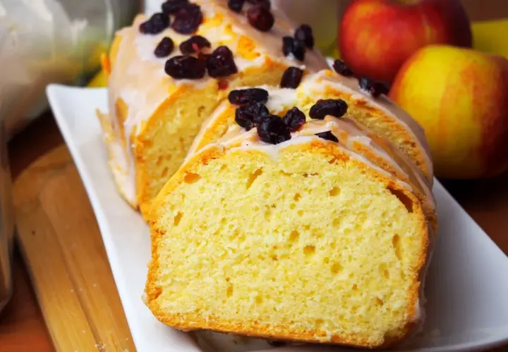 Pyszna babka na oleju, polana lukrem i posypana żurawiną, obok jabłek.