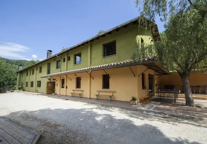 Edifici verd i groc amb taules de ping-pong i bancs a l'exterior. Un lloc ideal per a un refugi cap del rec.