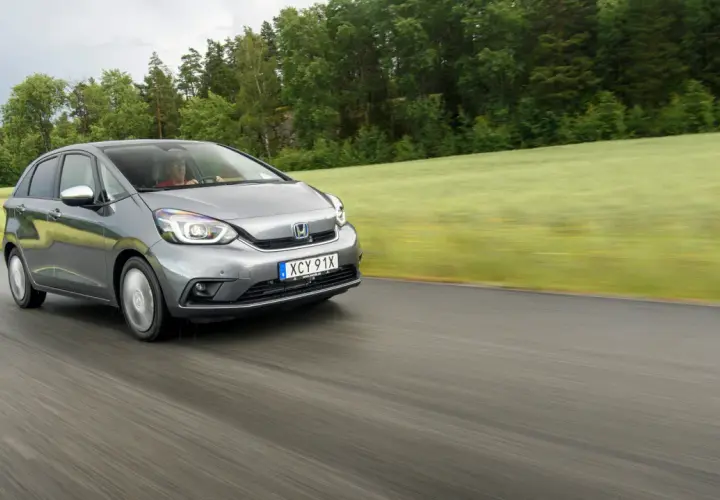 Grå Honda Jazz kör på en väg genom ett grönt landskap. Inga problem med denna bil, bara en härlig tur.