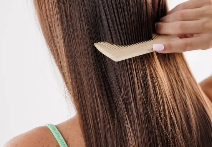 Peinando el pelo largo y castaño, que luce un poco apelmazado, con un peine de madera.