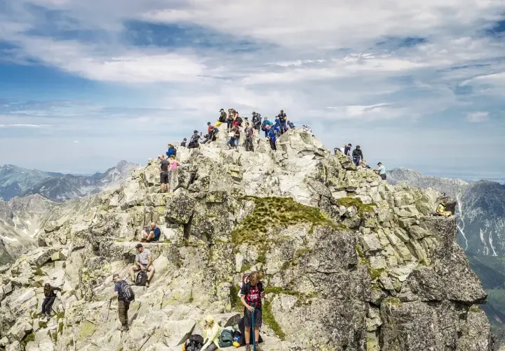 Tłum turystów na skalistym szczycie, najwyższy szczyt w Polsce, podziwia panoramę Tatr.