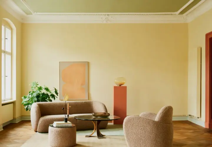 Ein Wohnzimmer mit gelben Wänden und einer grünen Decke, die frisch gestrichen wurde. Gemütliche Bouclé-Möbel und ein runder Couchtisch laden zum Verweilen ein.