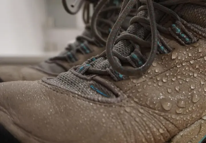 Close-up of tan hiking boots covered in water droplets, showing how to waterproof hiking boots effectively.