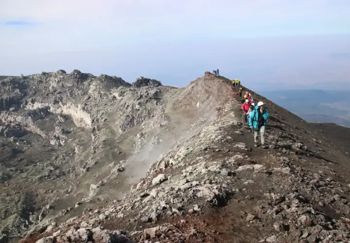 Escursionisti sul sentiero della cima Etna, tra rocce vulcaniche e fumo.