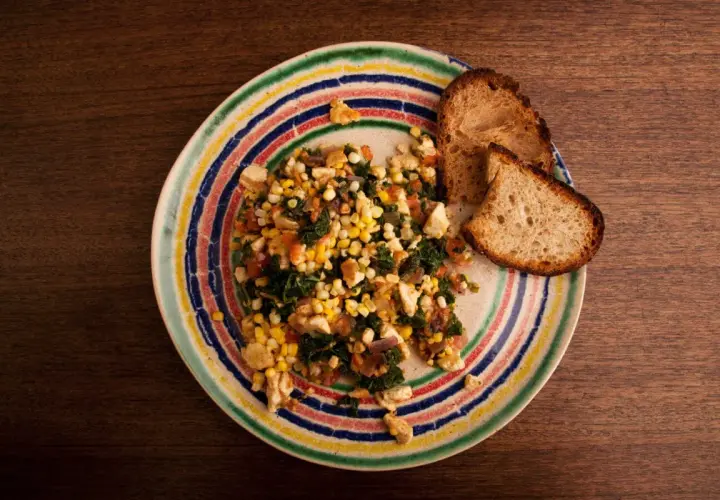 Revuelto de tofu con maíz y espinacas, servido con pan tostado en un plato colorido.