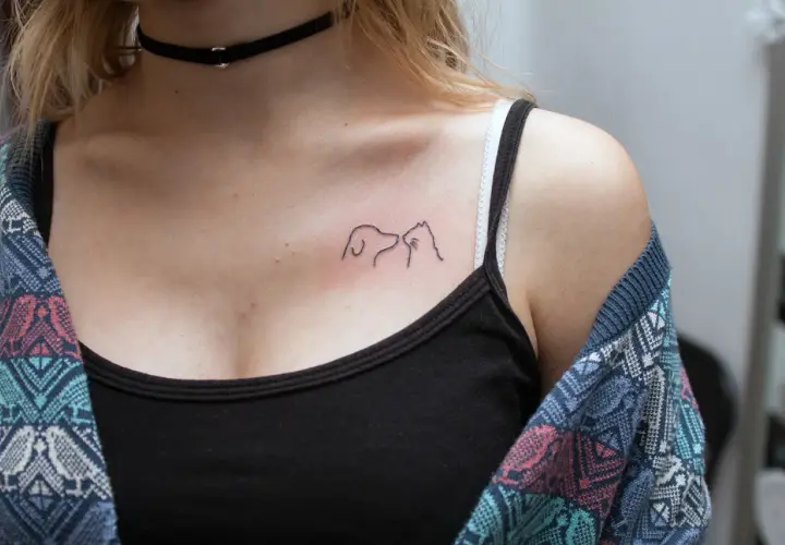 Minimalistyczny tatuaż pies i kot na dekolcie, symbol przyjaźni między gatunkami.