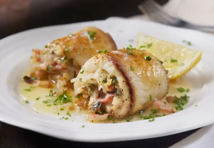 Involtini alla messinese ripieni di pesce e verdure, serviti su un piatto bianco con spicchio di limone e prezzemolo tritato.