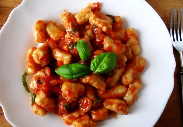 Pyszne gnocchi z sosem pomidorowym i świeżą bazylią na białym talerzu.