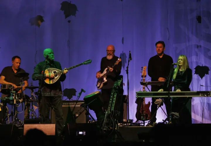 Zespół Dead Can Dance na koncercie. Muzycy grają na instrumentach, w tle fioletowa kurtyna z liśćmi.
