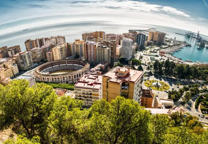 Widok na Malagę z lotu ptaka: arena, port, morze i budynki. Idealne miejsce na wakacje, warto zaplanować loty do Malagi.