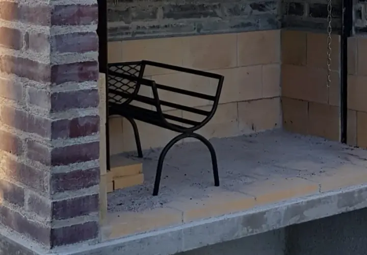 En delvis färdigbyggd grill av tegelstenar. En svart metallbänk står inne i utrymmet.