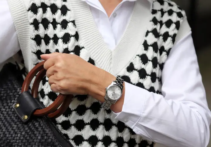 Elegancki zegarek na sztywnej bransolecie, dopełniający stylizację z białą koszulą i kamizelką w czarno-białe wzory.