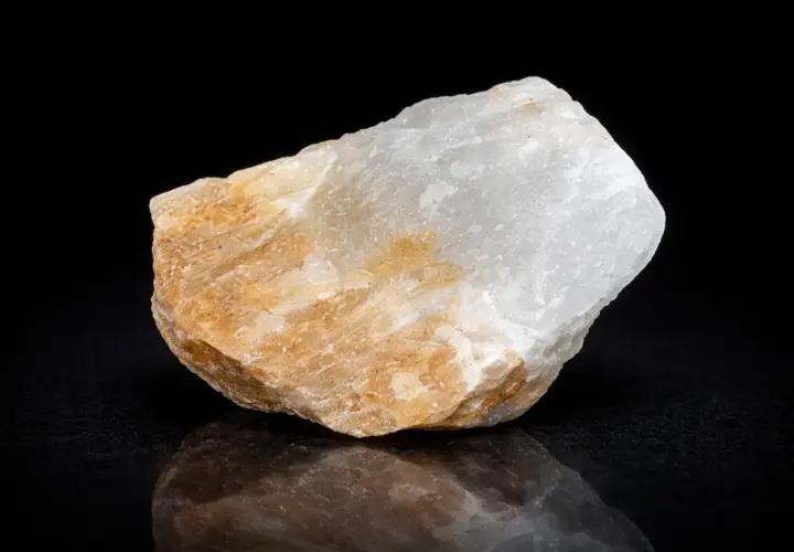 Ein Stück Alabaster, dessen Bedeutung in seiner Reinheit und seinem sanften Glanz liegt, schimmert in Weiß und Beige vor schwarzem Hintergrund.